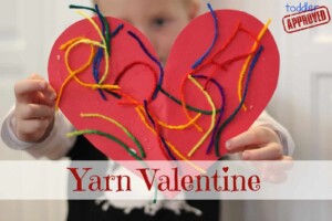 boy holding red construction paper heart with colorful yarn glued to it