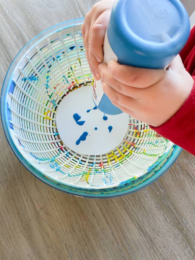 kid squeezing blue paint into the salad spinner