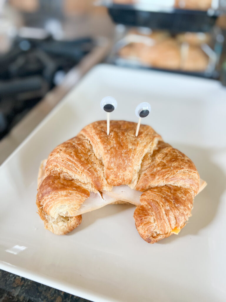 croissant sandwich that has googly eyes in it to look like a crab